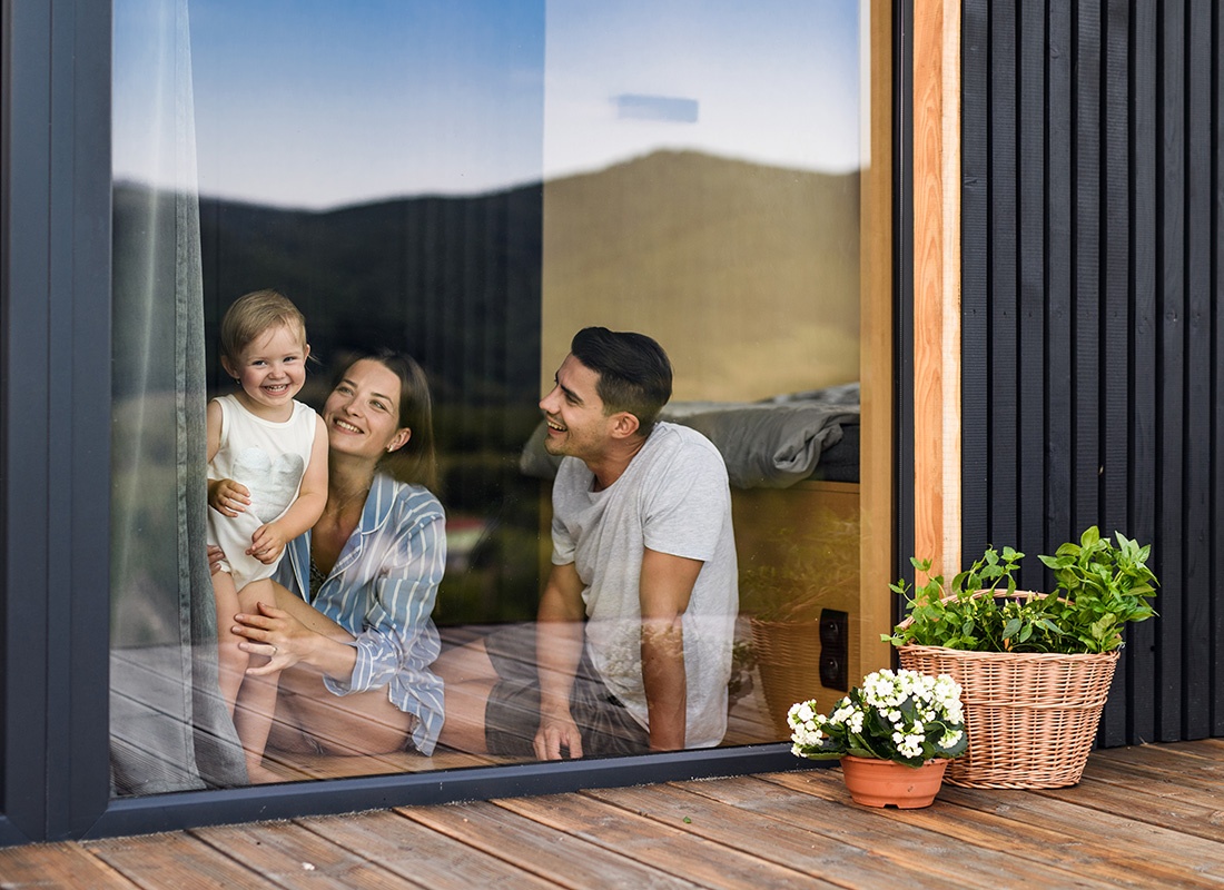 Employee Benefits - Portrait of Cheerful Young Parents Spending Time with Their Daughter Looking Out the Glass Floor Length Windows at Home